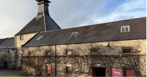 Aberfeldy distillery: het huis + huis met klein torentje in schotse stijl en op de voorgrond een bord waarop Dewar's by Aberfeldy op staat